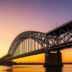 Obraz premium A massive steel arch bridge spans across a wide river under a golden sunset sky, showcasing intricate industrial architecture and engineering, iron, connection, transit