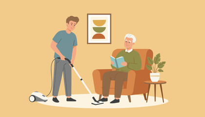 Fototapeta premium Young male caregiver vacuuming the carpet floor while an elderly man relaxes in an armchair reading a book at home.