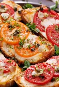 Grilled sourdough bread sandwiches, bruschettas with mozzarella and grana padano cheese, tomatoes, capers and garlic seasoned with aromatic herbs, close-up view