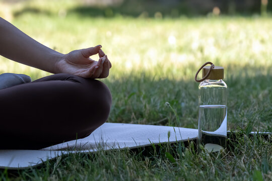 Woman practicing yoga meditation outdoors in a peaceful park with reusable water bottle. Mindfulness, hydration, healthy lifestyle, relaxation, wellness and self care concept.