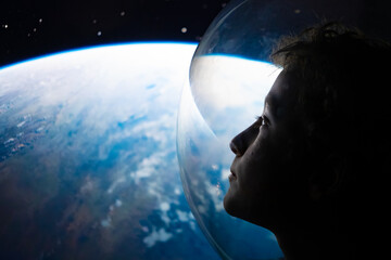 Conceptual close-up portrait of a young boy astronaut in a glass helmet looking out at planet Earth from outer space © Stefano Pessina