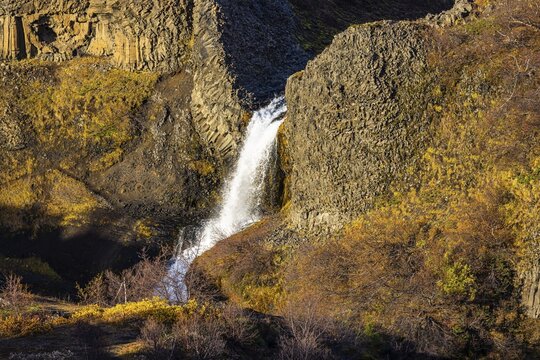 Small foaming waterfall cascading from a rock face, in the evening light, Sudurland, Iceland