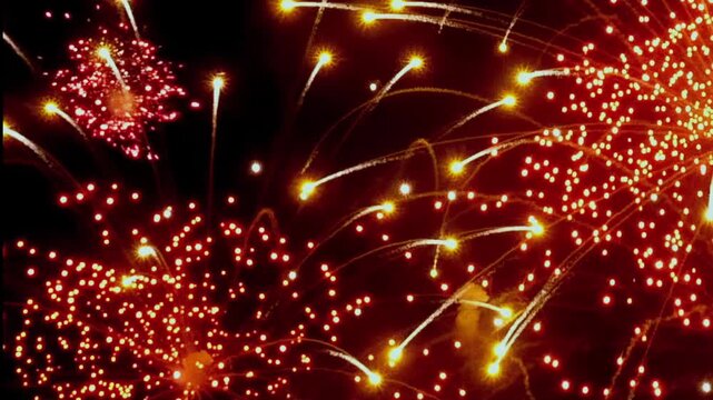 Brilliant red fireworks explode, painting streaks across night sky. Celebratory sparks shower down like falling stars. It is jubilant New Year Eve celebration shimmering lights and festive explosions.
