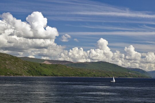 Single sailing boat on the sea, surrounded by a mountain landscape, under a sky with many clouds, ferry Oban, Mull, Scotland, Great Britain