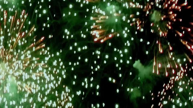 Glimmering green and radiant red fireworks illuminate the night. An artistic display of light and color erupts against the dark canvas of the evening sky.