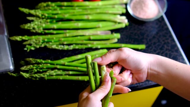 Female hand trimming fresh asparagus by snapping off tough ends before cooking preparing tender green spears for healthy homemade meals and simple recipes
