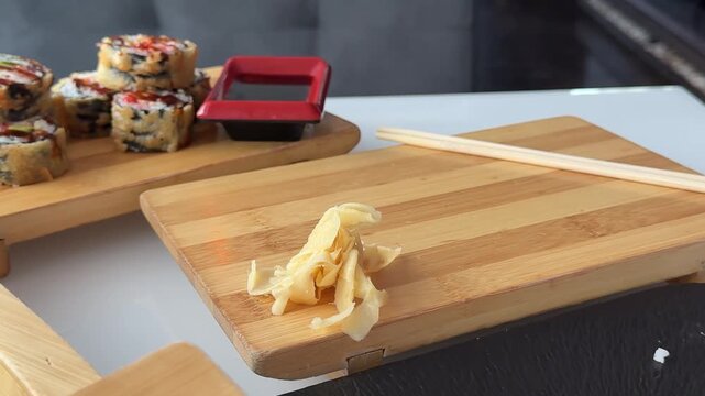 Close view of chef hands adding delicate slices of pickled ginger beside sushi rolls to complete an elegant asian food display