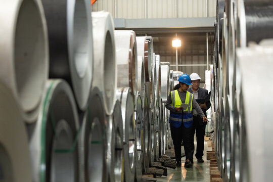 Professional logistics team auditing metal coil storage facility or checking inventory in warehouse.