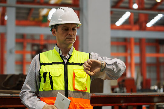 Engineer checking time on watch at industrial factory floor. Project management and deadline control in construction and manufacturing industry concept.