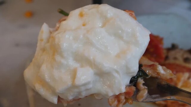 close-up of a traditional Italian pizza slice topped with a large, creamy ball of fresh burrata cheese, vibrant tomato sauce, and fresh basil leaves. The image captures the rich, soft texture of the c