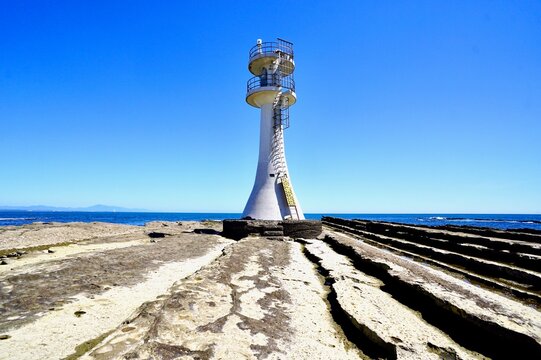White Aoshima Lighthouse standing on the fluted rock formation under blue sky