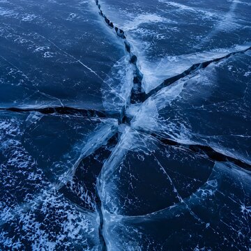 Ice cracking along frozen lake surface overhead blue hour shot of winter break