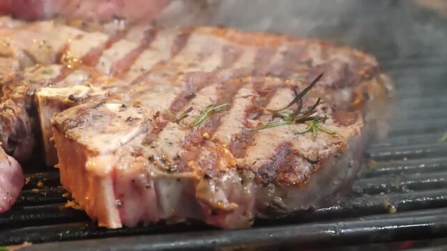 Close-up of a premium beef T-bone steak roasting on a hot barbecue grill. The meat features perfect grill marks and is seasoned with a sprig of fresh rosemary, with steam and smoke rising from the hea