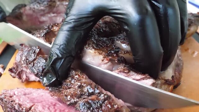Close-up footage of a chef wearing black gloves carefully slicing a perfectly grilled medium-rare beef steak on an outdoor cutting board. The meat shows a rich charred crust and tender pink center, hi