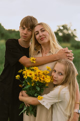 Fototapeta premium Mother and children embracing in a field with a bouquet of yellow flowers
