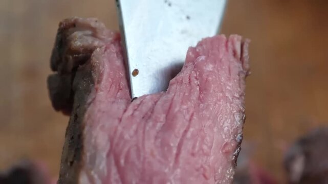 Extreme close-up footage of a sharp chef's knife slicing through a perfectly seared, tender ribeye steak. The shot highlights the rich pink medium-rare center, succulent texture, and savory meat fiber