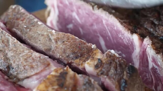 A professional chef in black gloves uses a sharp kitchen knife to slice through a perfectly grilled, thick-cut beef steak. The footage highlights the juicy, pink medium-rare interior and the savory ch