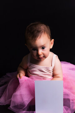 Baby girl learning ballet holding blank card on black background