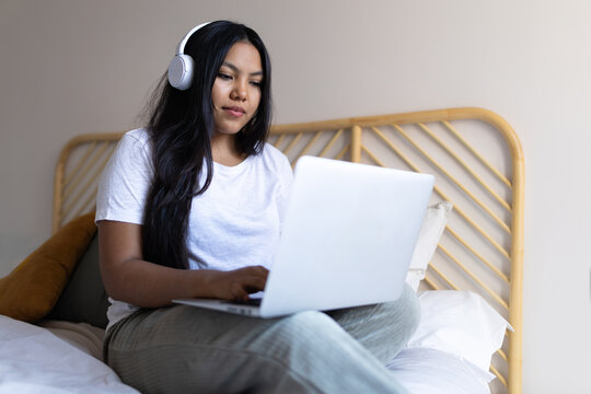 Latin woman working remotely from home using laptop and headphones