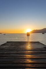 Naklejka premium Beautiful sunrise at São Francisco Beach Pier in São Sebastião, Brazil, with calm sea, golden reflections, and panoramic views of Ilhabela and Ubatuba. 