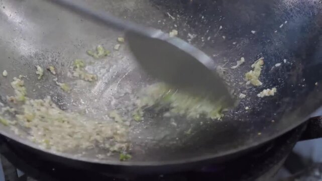 A dynamic close-up shot capturing the sizzle of minced garlic and ginger as they are saut&eacute;ed in a traditional metal wok with hot oil. Rising steam and motion highlight the intense heat and aroma of th
