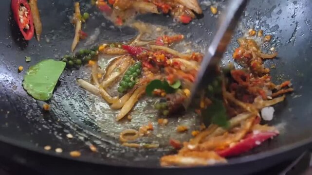 close-up, high-action shot of a chef expertly tossing ingredients in a traditional black wok. The footage captures the sizzling process of preparing a spicy Asian dish, featuring tender beef strips, f