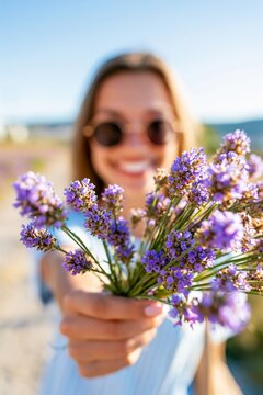 Happy woman holding a fresh lavender bouquet toward the camera with shallow depth of field