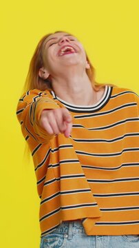 Caucasian woman pointing finger to camera, laughing out loud, taunting making fun of ridiculous appearance, funny joke anecdote, bullying, abuse. Young adult girl isolated on yellow background indoors