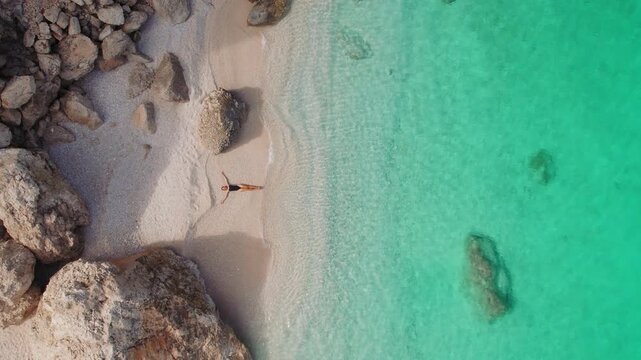 Woman relaxing alone on a hidden sandy cove beach with turquoise sea water in summer