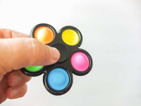 Hand holding a black flower shaped pop it fidget spinner toy on white background.