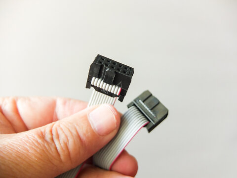 Hand holding a gray flat ribbon IDC cable with black connectors close up.