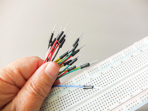 Hand holding a bunch of colorful jumper wires next to an electronic breadboard.