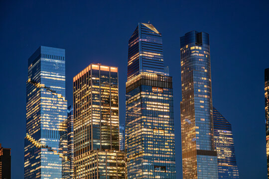 Hudson Yards skyscrapers against deep blue Manhattan night sky. Upper sections of illuminated glass towers fill a horizontal frame with clear sky and sparse stars.