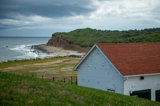 Coastal bluffs and oil house at Montauk Point. White masonry structure and red roof frame a rocky shoreline beneath dark clouds.