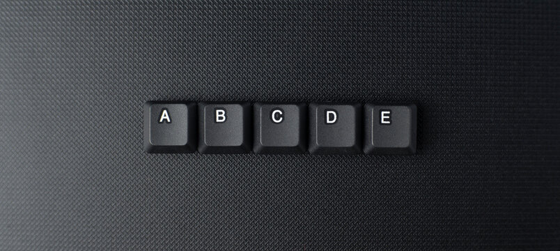 ABCDE letters arranged neatly from keyboard keycaps on a dark background, suitable for alphabet learning, reading, basic education, and language concepts.