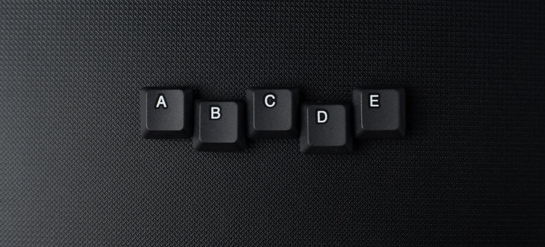Uneven ABCDE keyboard key arrangement on a dark surface, representing alphabet learning, creativity, education, typography, and digital communication.