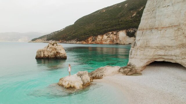Cephalonia cove view with woman on rock framed by cliffs and bright turquoise sea, summer Greece