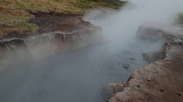 Steam rising from a bubbling geothermal mud pot in a volcanic landscape under cloudy skies in Seltun Geothermal Area Krysuvik Iceland