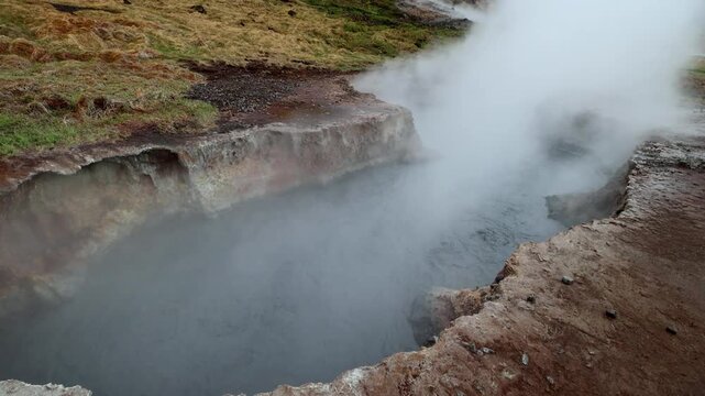 Geothermal mud pot boiling and emitting steam under overcast skies in Seltun Geothermal Area Krysuvik Reykjanes Peninsula Iceland