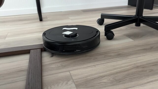 A robot vacuum cleans around the computer chair and armchair at home and in the office.