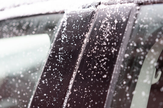 Close-up of a car door and window lightly covered with snowflakes.