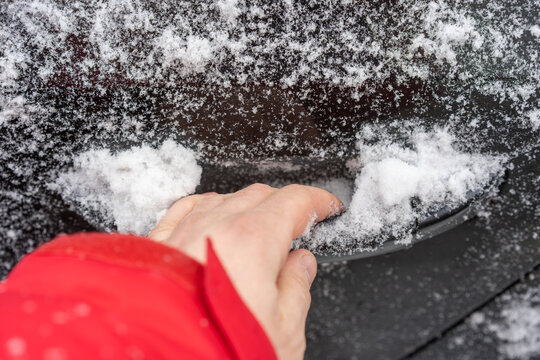 Close-up of a hand in a red sleeve reaching for a car door handle partially buried under fresh snow.
