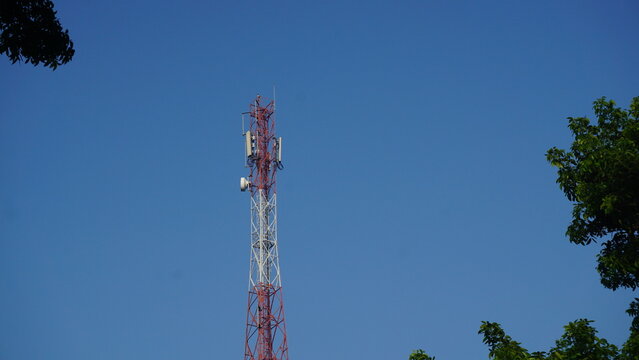 A towering red and white telecommunications antenna tower against a blue sky.