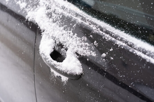 Close-up of a dark car door with a handle partially filled and covered by fresh snow.