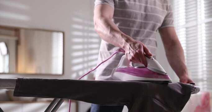 Man ironing t-shirt on board at home, closeup
