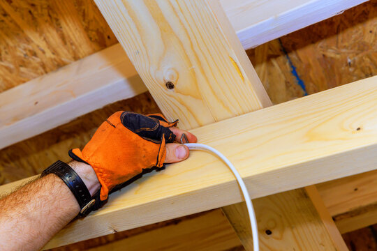 Worker installs electrical wire in wooden beams at construction site