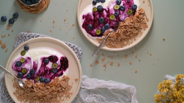 A flat lay overhead view of rustic ceramic plates featuring thick creamy yogurt swirled with vibrant berry compote and topped with fresh blueberries. Soft natural lighting creates a calm, aesthetic mo