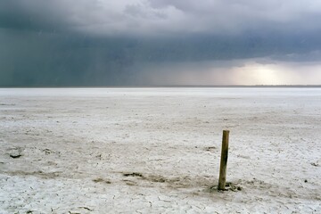 Fototapeta premium Lone Wooden Stake on Salt Flat During Sudden Hailstorm