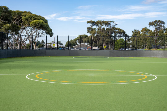 An empty synthetic sports field with center circle markings sits enclosed by fencing in suburban Melbourne Australia. Community sports facilities, local council infrastructure, recreational amenities