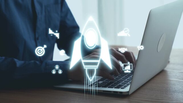 A man works on a laptop in a modern workspace, highlighting themes of innovation and growth through a digital rocket symbol, reflecting business strategies and future possibilities. Qubit